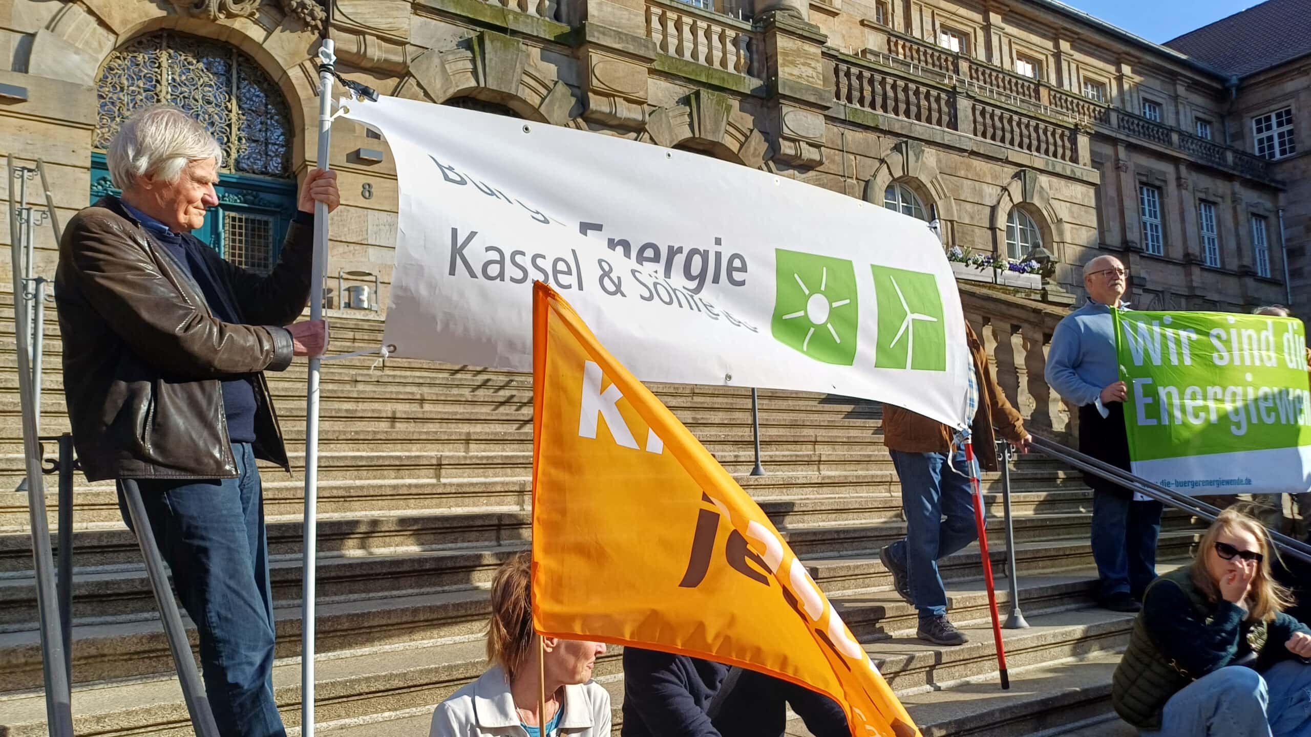 Demonstranten mit Bannern für Bürgerenergie Kassel & Söhre eG vor dem Rathaus.